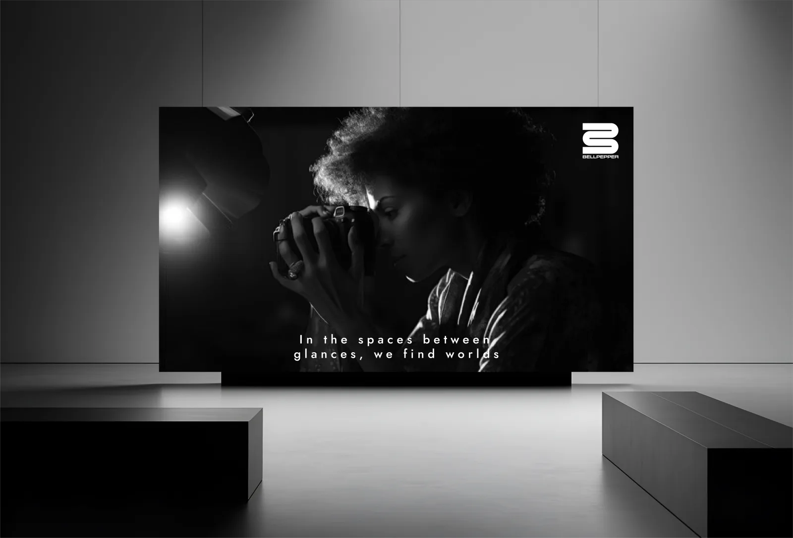 Bellpepper Media brand film on a gallery screen, a photographer mid-shot with the tagline "In the spaces between glances, we find worlds"